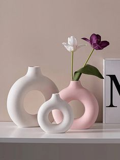 three white and pink vases with flowers in them sitting on a shelf next to a letter m