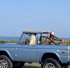 two women are sitting in the back of a blue truck with large tires and one woman is wearing a red hat