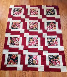 a red and white patchwork quilt on the floor with flowers all over it's edges