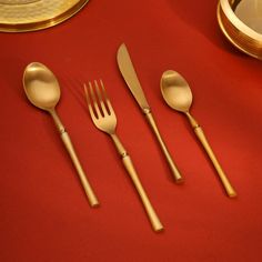 four forks, two spoons and one knife on a red tablecloth with gold plates