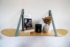 a shelf with books, vase and candle on it next to a wall mounted book rack