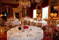 a dining room with tables and chairs covered in white tablecloths, gold chandeliers and candles