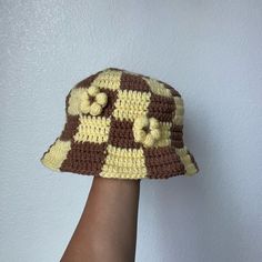 a crocheted brown and yellow hat on someone's hand with white wall in the background