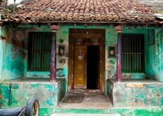 a motorcycle parked in front of an old building with green paint and red roof tiles