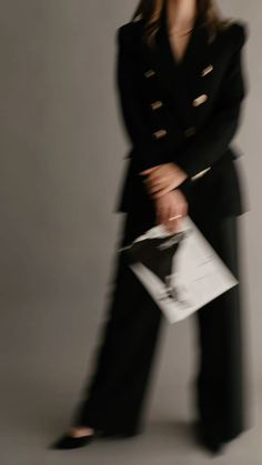 a woman in black is walking with her hands on her hips and holding a folder