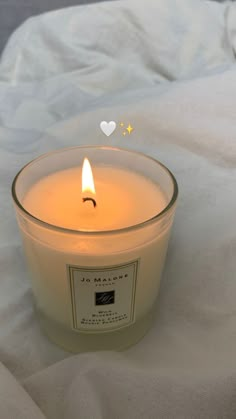 a lit candle sitting on top of a white sheet covered bed next to a heart