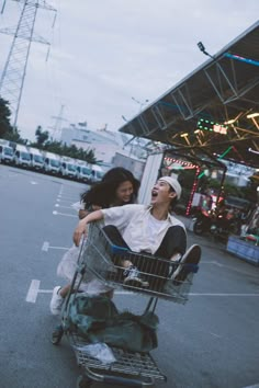 two people sitting in a shopping cart on the side of the road with their arms around each other