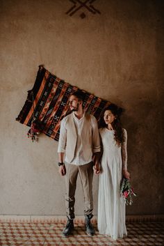 a man and woman standing next to each other in front of a wall with a rug on it