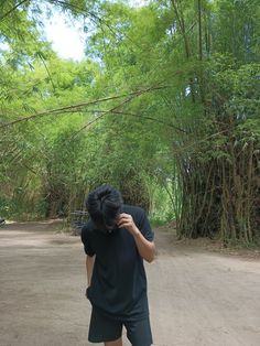 a person standing in the middle of a dirt road next to some trees and bushes