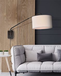 a white couch sitting in front of a wooden wall with a lamp on top of it