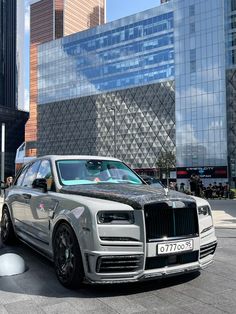 a silver car parked in front of a tall building next to other buildings and people