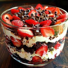 a dessert with strawberries, chocolate chips and cream in a glass bowl on a wooden table