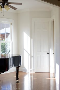 an empty room with a piano in the corner and a ceiling fan hanging from the ceiling