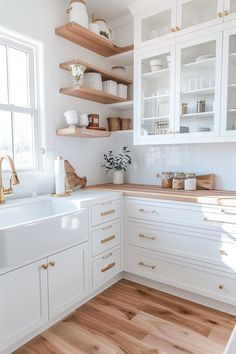 a kitchen with white cabinets and wood flooring is pictured in this image, there are shelves on the wall above the sink