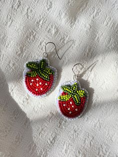 two red and green beaded strawberry earrings sitting on top of a white cloth covered surface