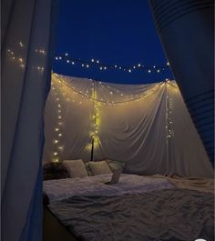 a bed covered in white sheets with lights on the ceiling and curtains over it's headboard