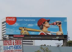 a billboard with a man holding a baseball bat and drinking coca - cola on it