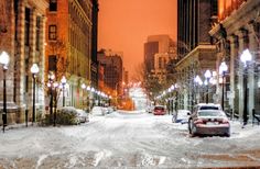 a city street is covered in snow during the night time, with cars parked on both sides