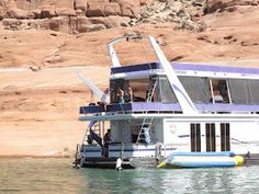 a house boat floating on top of a lake next to a rocky cliff covered hillside