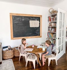 two children sitting at a table in front of a chalkboard