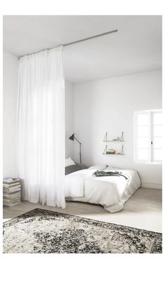 a bedroom with white walls and flooring has a large rug on the floor next to the bed