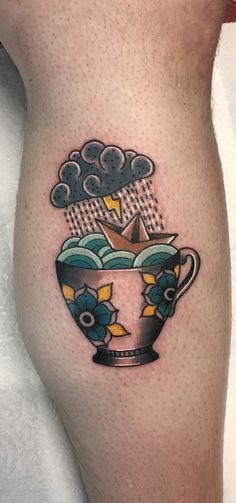 a small tattoo on the leg of a person with an origami boat in a cup