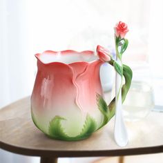 a pink and green vase sitting on top of a table next to a white spoon