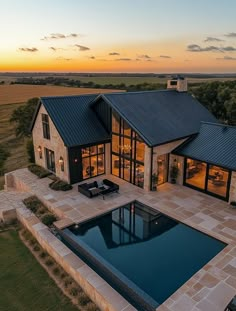 an aerial view of a house with a pool in the foreground and a sunset behind it