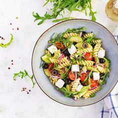 a bowl filled with pasta salad next to a glass of wine and some greens on the side