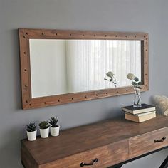 a mirror on the wall above a wooden table with two potted plants and a book