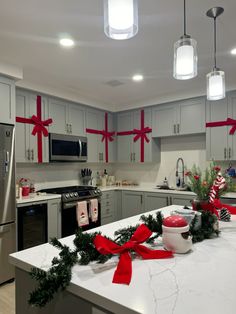 a kitchen decorated for christmas with red bows on the counter and lights hanging from the ceiling