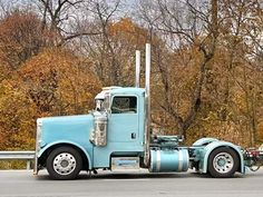 a large blue semi truck parked on the side of a road next to some trees