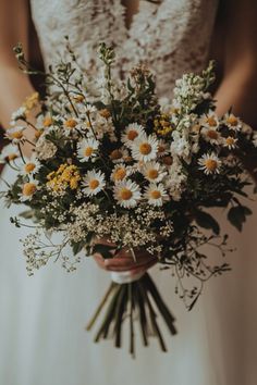 a bride holding a bouquet of daisies and wildflowers