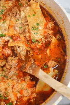 a large pot filled with meat and vegetable soup next to a wooden spoon on top of a table