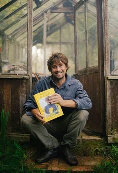 a man sitting in front of a greenhouse holding a book