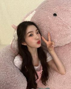 a woman laying on top of a giant pink teddy bear with her hand in the air