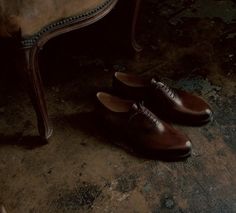 a pair of brown shoes sitting on top of a wooden floor next to a chair