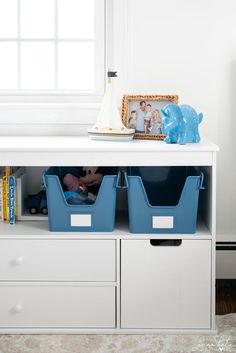 two blue bins sit on top of a white shelf