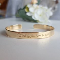 a gold bracelet with the words walk by faith and my spirit engraved on it next to a white flower