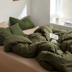 an unmade bed with green sheets and pillows in a white room next to a window