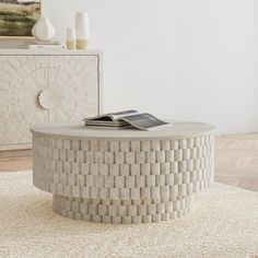 a round coffee table sitting on top of a rug in front of a white wall