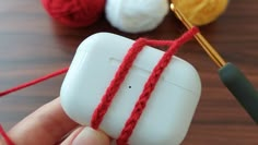 a hand holding an object with yarn on it and crochet needles in the background