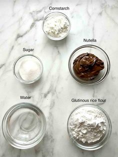 ingredients to make chocolate cake in glass bowls on a white marble countertop with text below