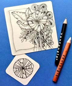 a pencil and some drawings on a blue table next to two small cards with designs