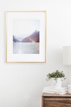 a framed photograph hangs on the wall next to a nightstand with a lamp and potted plant