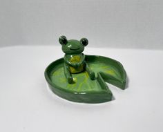 a green frog figurine sitting on top of a leaf shaped tray with eyes wide open