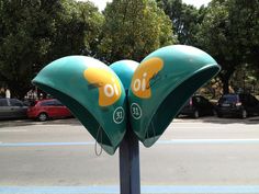 two green and yellow flower shaped signs on a pole near a street with cars parked in the background