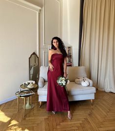 a woman in a red dress standing next to a couch