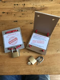 an open padlock and two keys on a wooden table next to a box with a lock