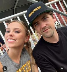 a man and woman sitting next to each other in front of a metal fence at a sporting event